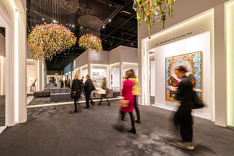 Visitors walking through a modern art gallery with colorful chandeliers and large paintings in a well-lit exhibition space.