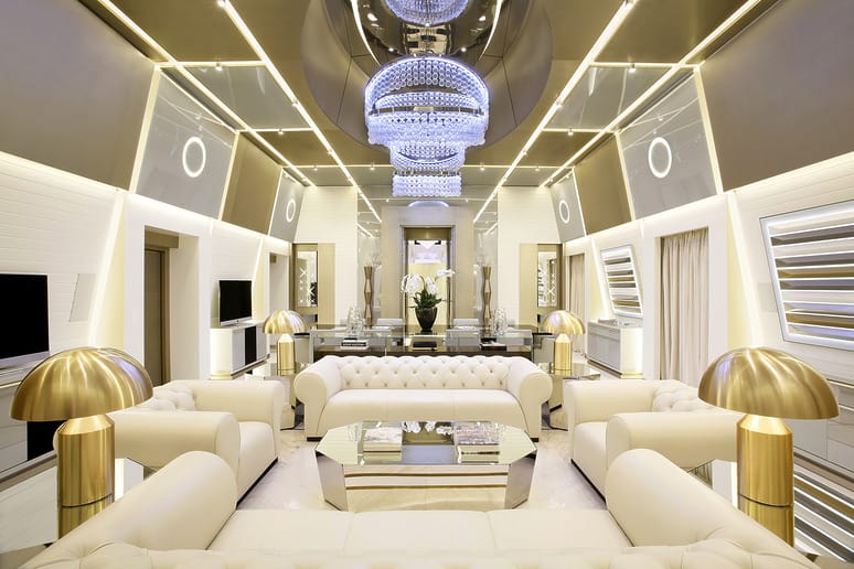 Milan hotel Excelsior's luxurious modern living room with elegant white sofas, gold accents, and a large crystal chandelier.