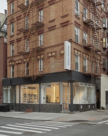 Corner view of a brick building with large windows and fire escapes, displaying a retail store on the ground floor.