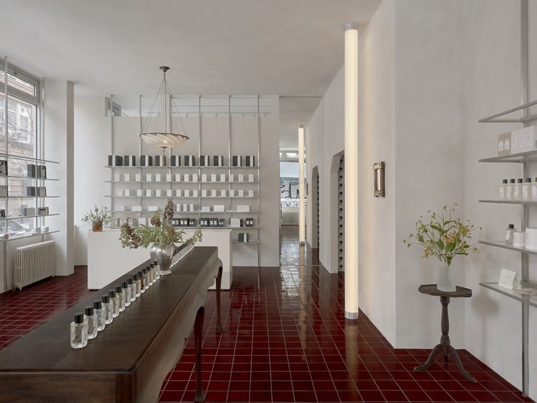 Modern perfume store interior with red-tiled floor, wooden table displaying bottles, and shelves with neatly arranged products.