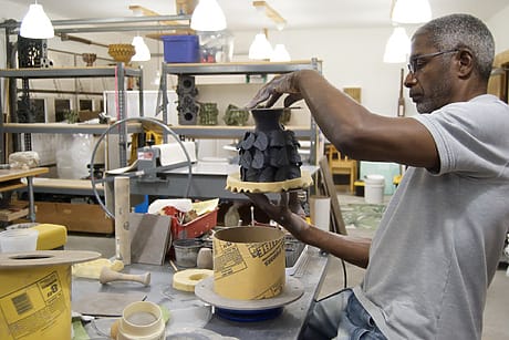 Man crafting ceramic piece in a workshop surrounded by pottery tools and materials.