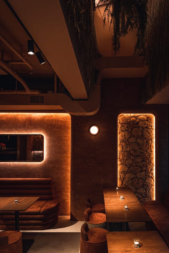 Dimly lit, cozy restaurant interior with wooden tables, cushioned seating, and soft wall lighting for an intimate atmosphere.