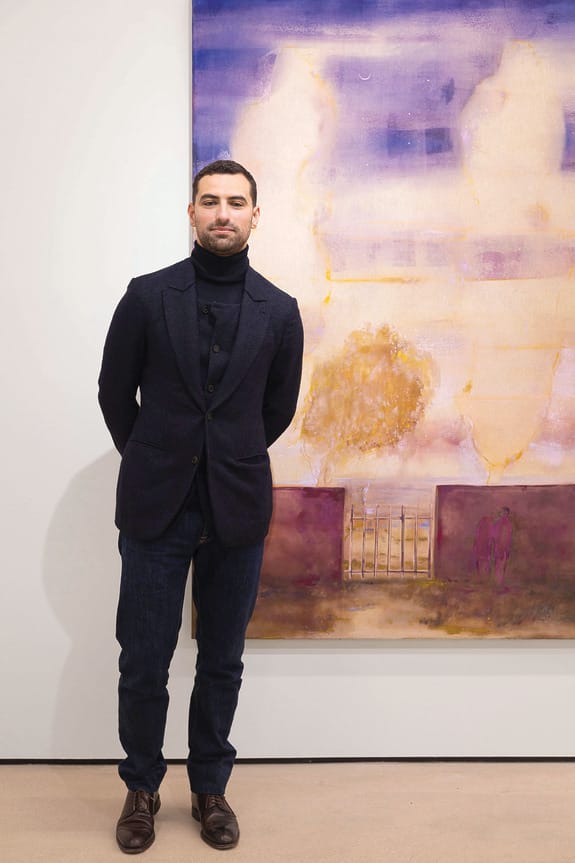 Person standing in front of a large abstract painting with purple and beige tones in a gallery setting.