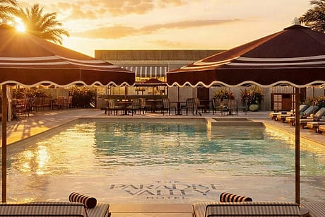Hotel pool at sunset with lounge chairs and umbrellas lining the poolside, surrounded by palm trees.