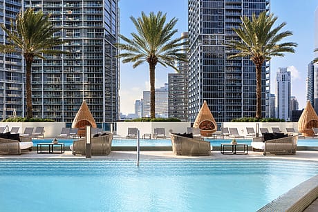 Modern city skyline view with palm trees and poolside lounge chairs at swimming pool at Kimpton EPIC Miami.