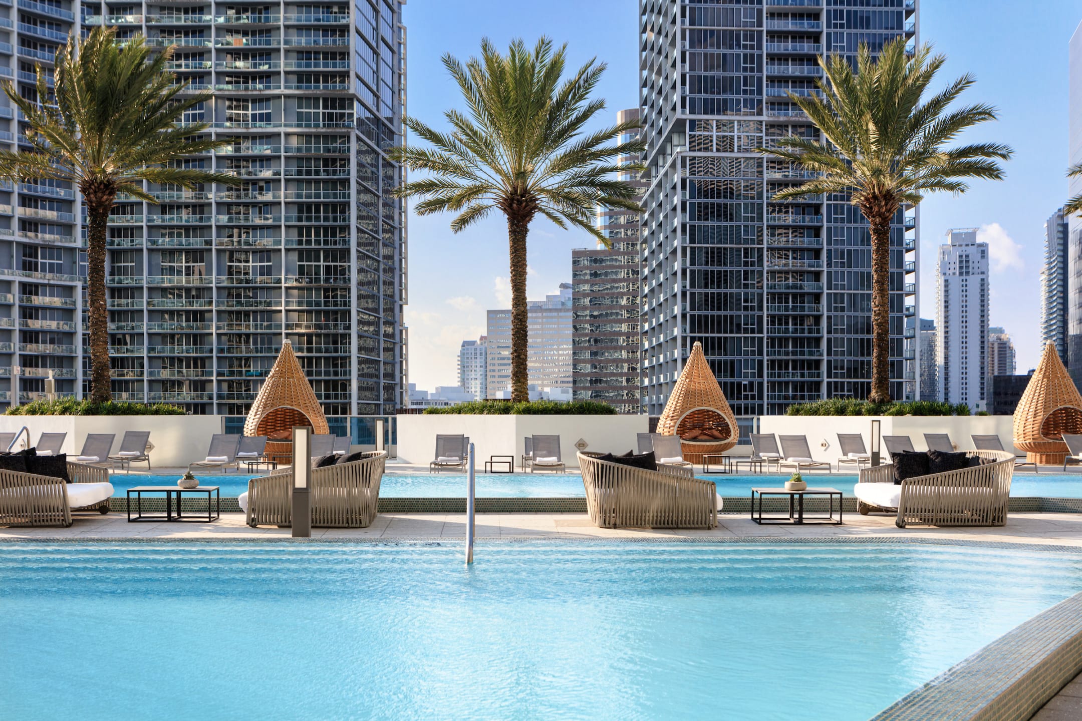 Modern city skyline view with palm trees and poolside lounge chairs at swimming pool at Kimpton EPIC Miami.