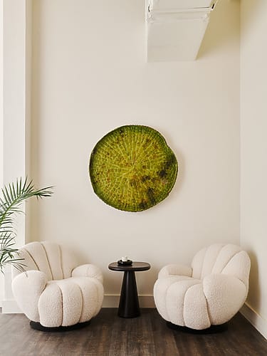 Modern lounge with two white chairs, a round table, and a large circular green wall art piece in a minimalistic room.