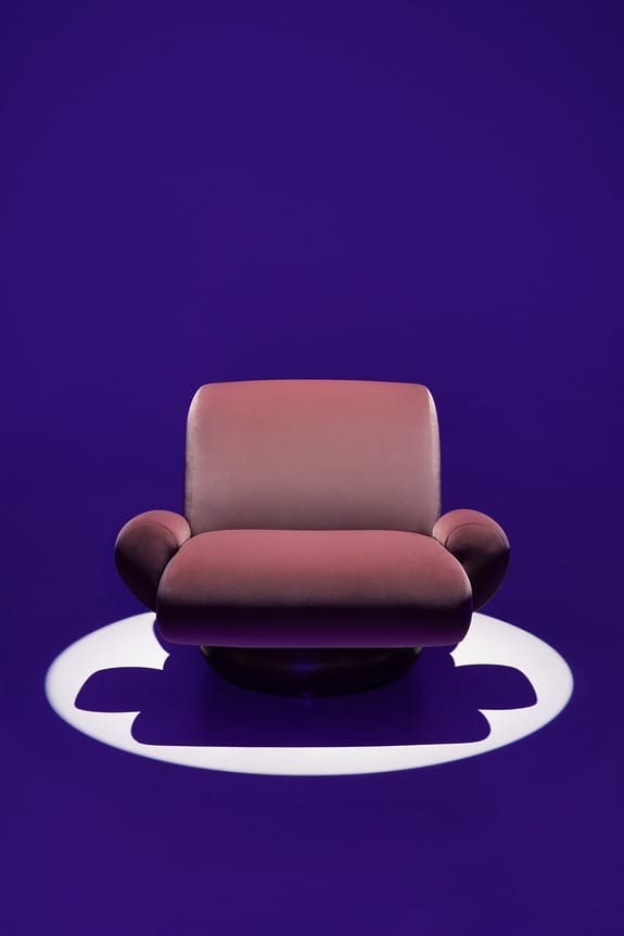 Pink modern armchair on a purple background with spotlight effect.