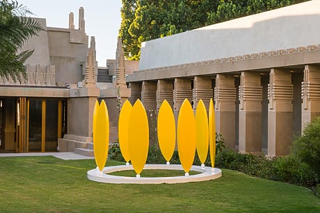 Yellow art installation on grass in front of a historic building with trees and architectural details in the background.