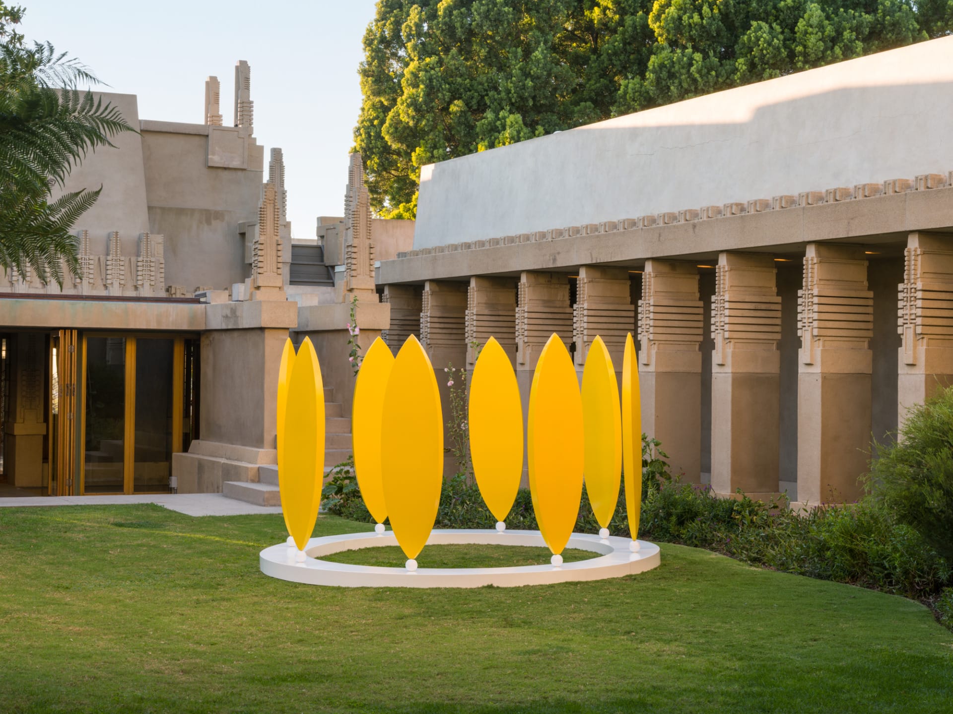 Yellow art installation on grass in front of a historic building with trees and architectural details in the background.