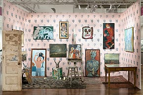 Art gallery display with eclectic paintings, pink patterned walls, ornate rugs, and wooden furniture creating an artistic ambiance.