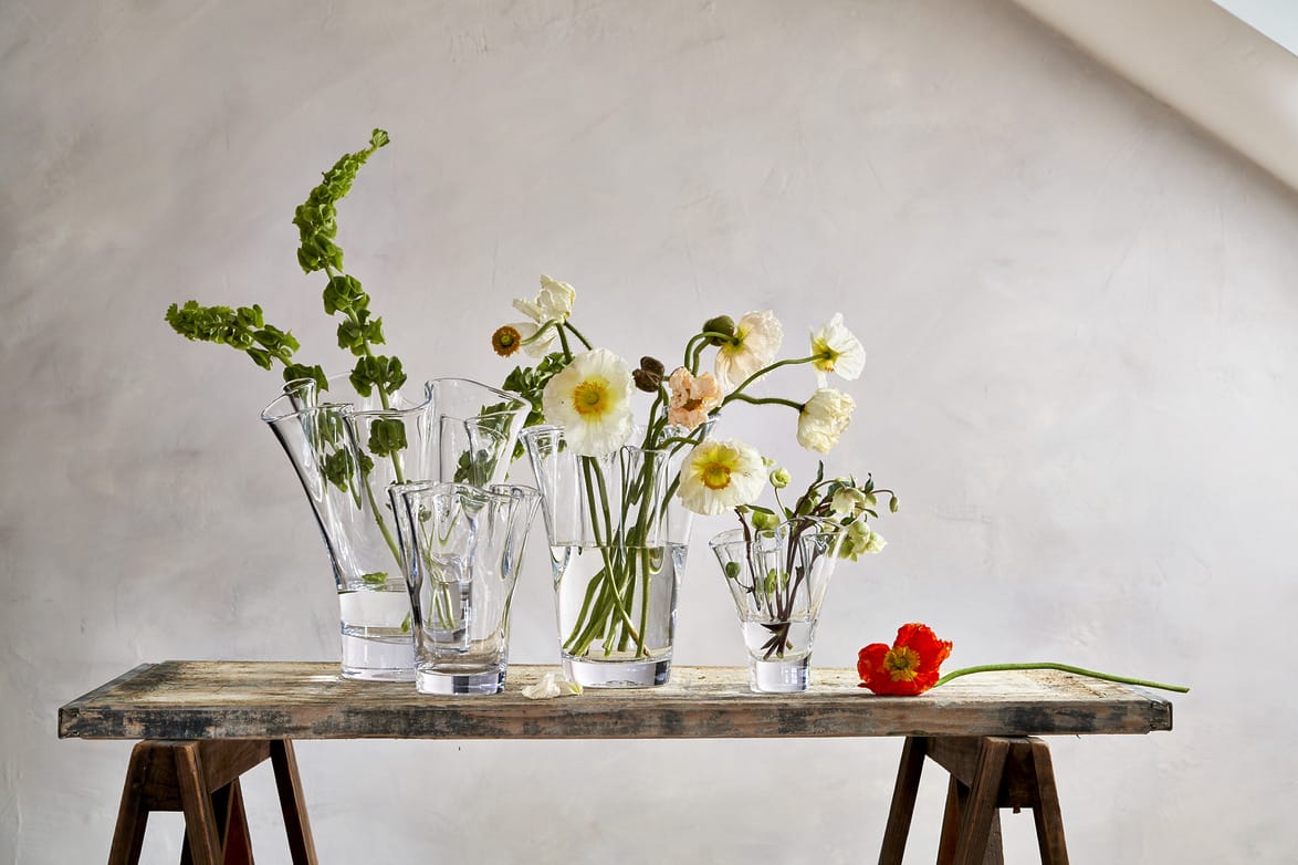Various flowers arranged in glass vases on a wooden table against a soft white background.