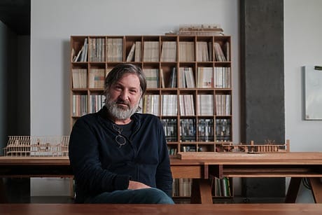 Man sitting in an office with bookshelves in the background, featuring architectural models on wooden tables.