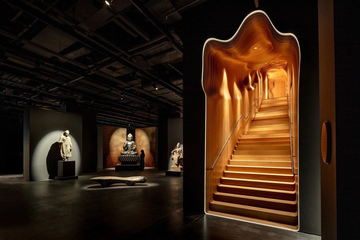 Art at Sotheby's Maison, Hong Kong in a modern interior with illuminated wooden staircase and sculptures in dimly lit exhibition space.