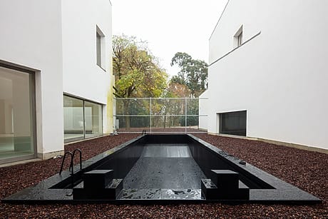 Modern minimalist outdoor pool surrounded by white buildings and trees in the background.