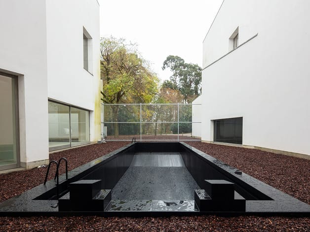 Modern minimalist outdoor pool surrounded by white buildings and trees in the background.