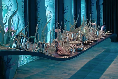 Elegant dining table set with crystal glassware and decorative elements against an artistic, ocean-themed backdrop.