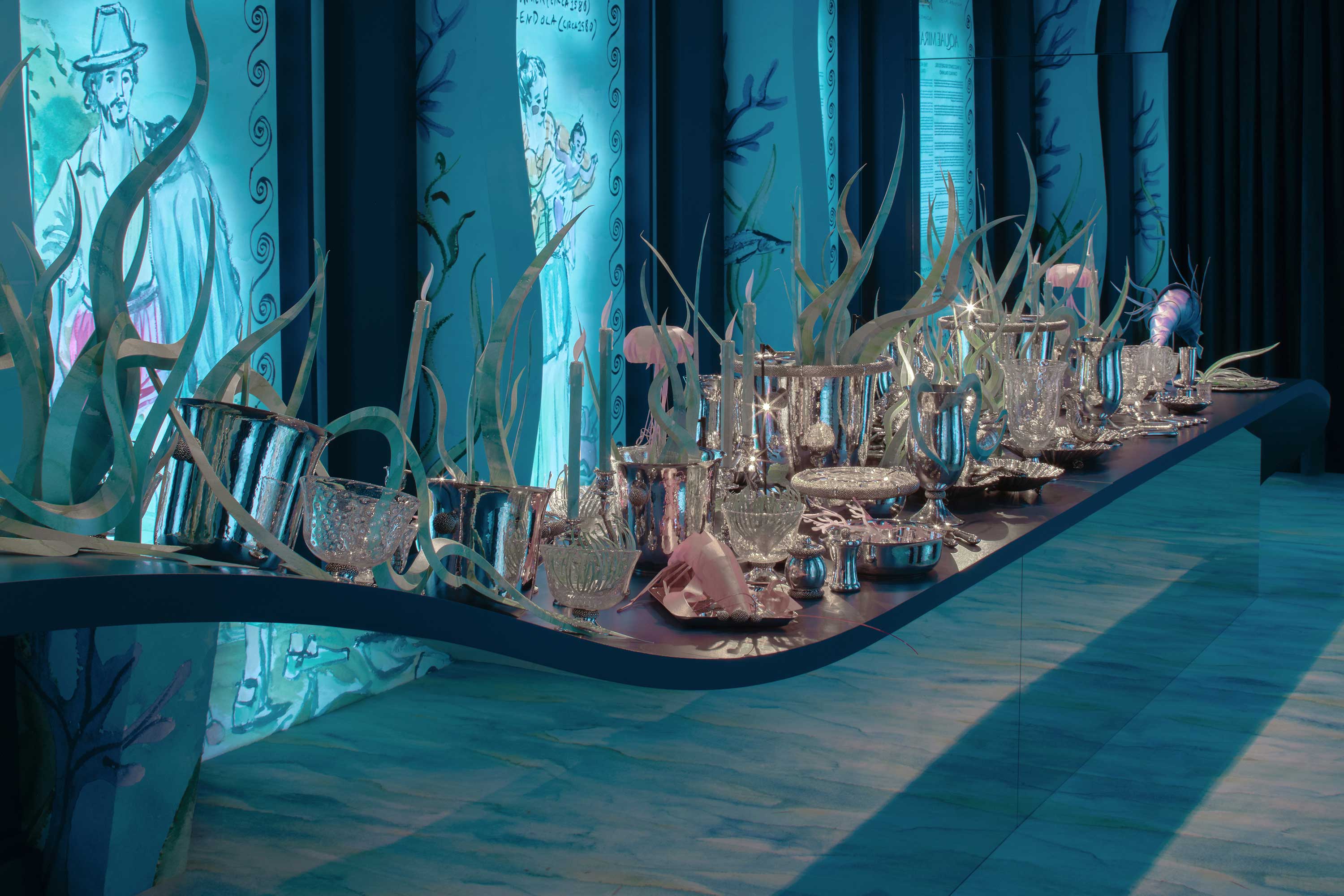 Elegant dining table set with crystal glassware and decorative elements against an artistic, ocean-themed backdrop.