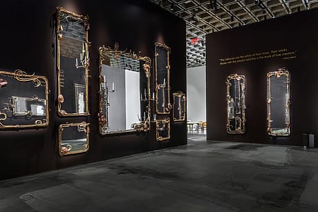 Art installation with ornate mirrors and dark walls in a gallery space with subtle lighting.