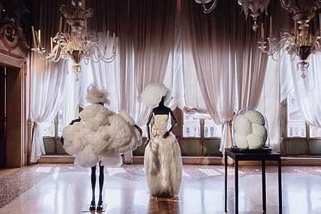 Elegant fashion display with avant-garde white dresses and chandeliers in a luxurious room with draped curtains.