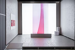 Modern art gallery with a large pink vertical installation, abstract paintings on walls, and minimalist seating against neutral tones.