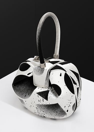 Abstract black and white handbag with curved handle and geometric pattern on a white surface.