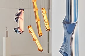 Colorful, abstract glass sculptures with twisting shapes hanging in a minimalistic white gallery space.