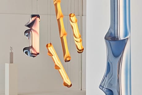 Colorful, abstract glass sculptures with twisting shapes hanging in a minimalistic white gallery space.