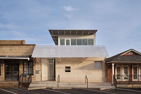 Modern building with large windows and a white awning, set between two traditional styled buildings under a blue sky.