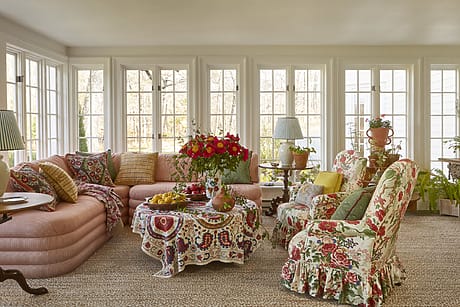 Cozy sunroom with floral upholstered furniture, large windows, and a colorful bouquet on a central table.