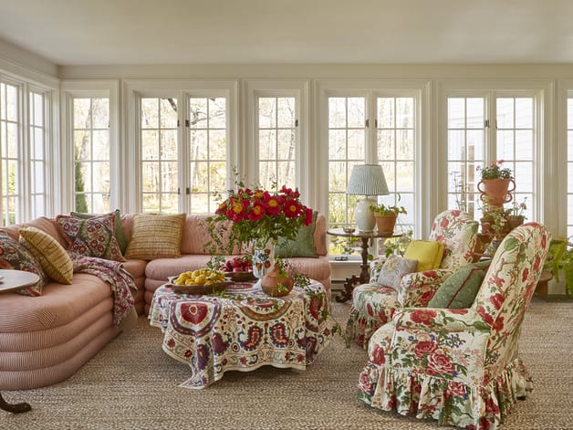 Cozy sunroom with floral upholstered furniture, large windows, and a colorful bouquet on a central table.