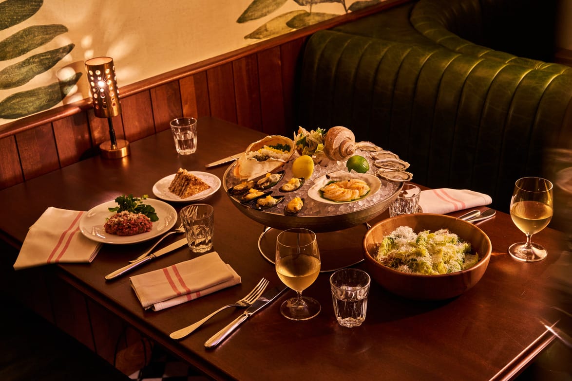 A table with seafood platter, tartare, salad, wine glasses, and a cozy dining setting.