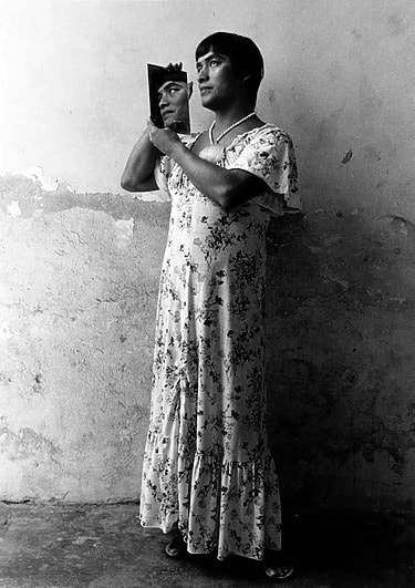 Graciela Iturbide's photograph of Magnolia in a floral dress holding a triangular mirror, standing against a textured wall.
