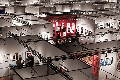 AIPAD exhibition with people viewing framed artwork on display in a large gallery space with overhead lighting at the Park Avenue Armory in New York.
