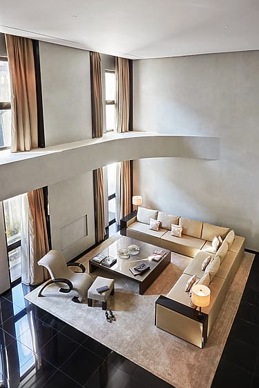 Spacious modern living room with high ceilings, sectional sofa, sleek furniture, tall windows, and warm lighting.