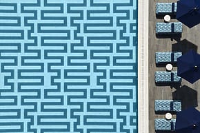 Aerial view of a patterned swimming pool beside lounge chairs and umbrellas on a sunny day.