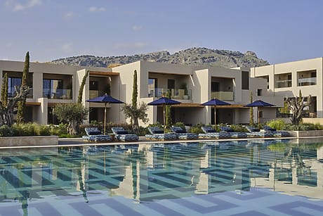 Modern luxury resort with a sparkling pool, sun loungers, and mountain backdrop on a clear day.