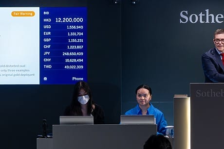 Auctioneer at Sotheby's with two assistants, leading a watch auction with bid details displayed on a screen.
