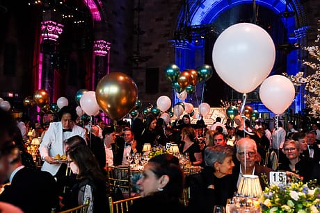 Elegant event with guests in formal attire, colorful balloons, and ambient lighting in a grand hall.