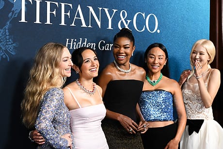 Five women in elegant dresses smiling at a Tiffany & Co. event, standing in front of a blue backdrop with branding.