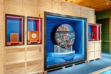Exhibition display at Hermes featuring vintage audio equipment with colorful backgrounds and wooden paneling.