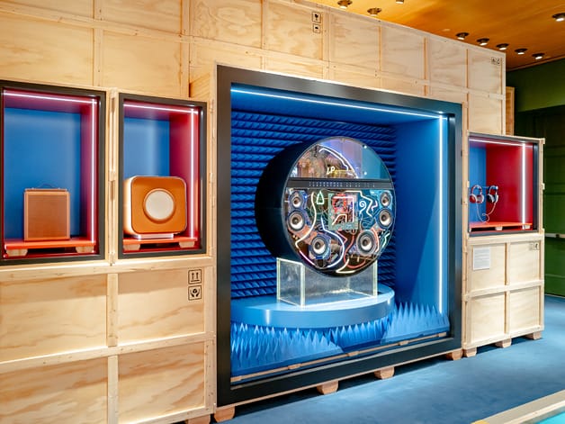 Exhibition display at Hermes featuring vintage audio equipment with colorful backgrounds and wooden paneling.