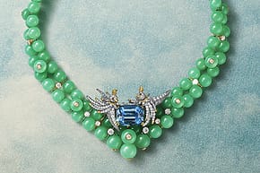 Green beaded necklace with a central blue gemstone and intricate silver detailing on a textured blue background.