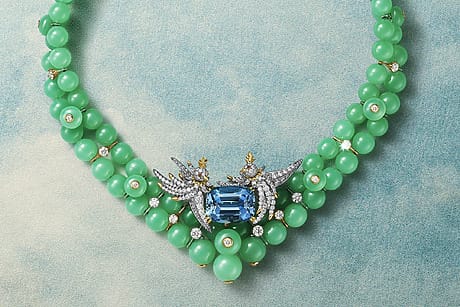 Green beaded necklace with a central blue gemstone and intricate silver detailing on a textured blue background.