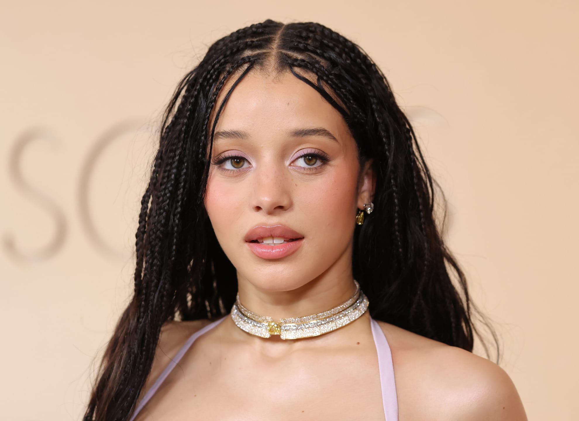Actress Chase Infiniti on the red carpet with braided hair wearing a choker necklace and a sleeveless top against a neutral background.