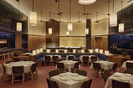 Elegant restaurant interior with round tables, cushioned seating, and modern pendant lighting.