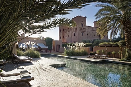 Luxury resort with a tranquil outdoor pool, palm trees, and historic architecture under a clear blue sky.