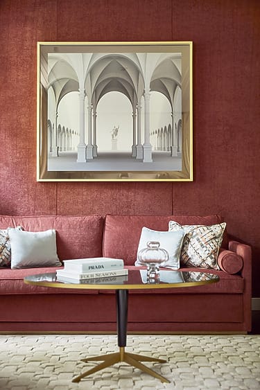 Room at Four Seasons Milano with terracotta sofa, decorative pillows, round glass coffee table, and framed architectural artwork on the wall.