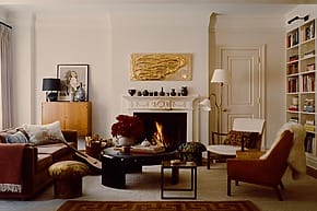 Chic living room with elegant furniture, a cozy fireplace, bookshelves, and a modern art piece above the mantel.
