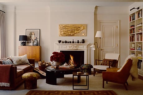Chic living room with elegant furniture, a cozy fireplace, bookshelves, and a modern art piece above the mantel.